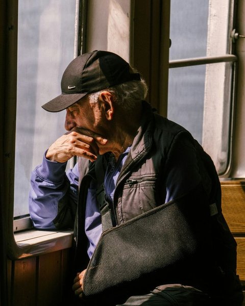A man sitting quietly with his arm in a sling, looking out a window